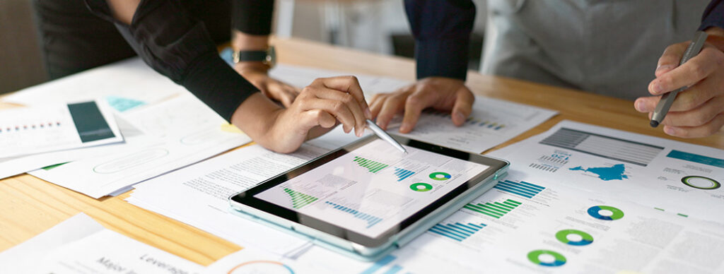 Two people looking at charts and graphs on a tablet, and sheets of paper.